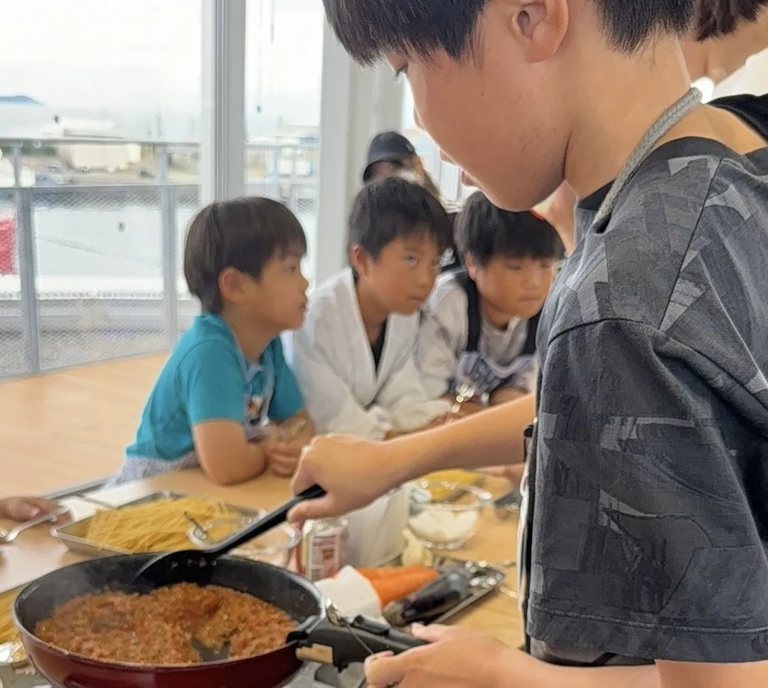 子どもたちが鍋でミートソースを煮込んでいる様子